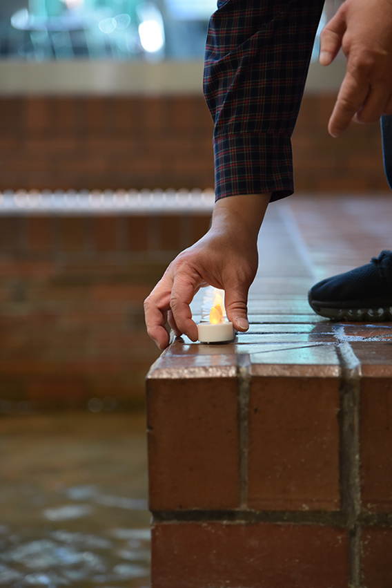 hand places the last memorial candle on the edge of the Atrium fountain