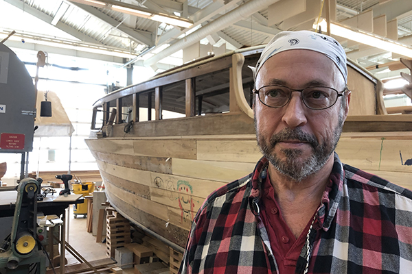 Chef Luke Rinaman poses in front of a practice boat at the Wood Technology Center