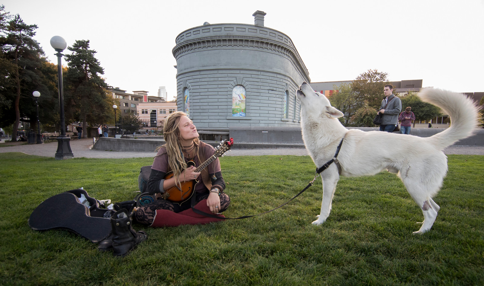a guitar player with long hear sings along with her white dog at Cal Anderson Park