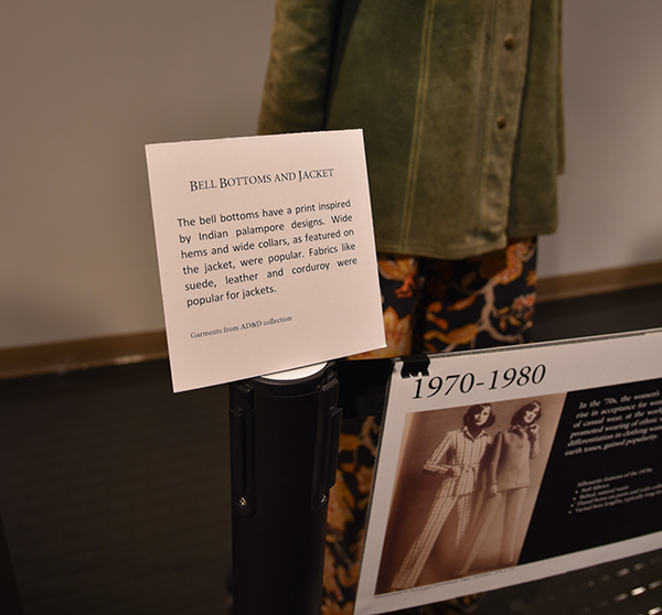  a sign in the gallery exhibit describes the fashion styles of the clothes on display