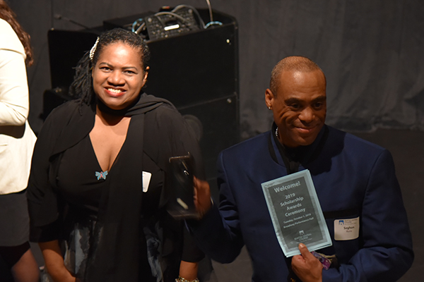 two students smile after a scholarship ceremony. One holds up the program from the event